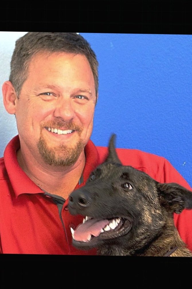 Steve Kotowske smiling beside a dark brindle shepherd